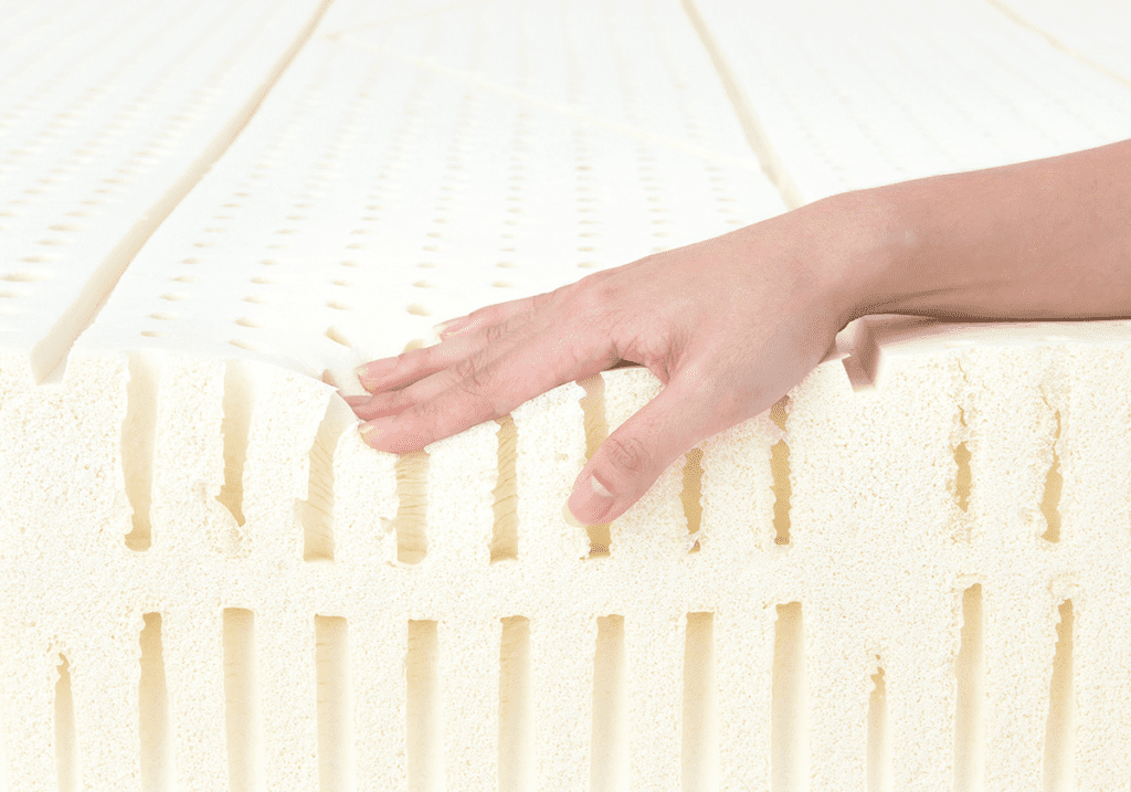 Close-up view of a hand touching the naturally breathable and hypoallergenic Heveya® Natural Latex Mattress III core. The open-cell structure promotes air circulation for a cool and comfortable sleep.