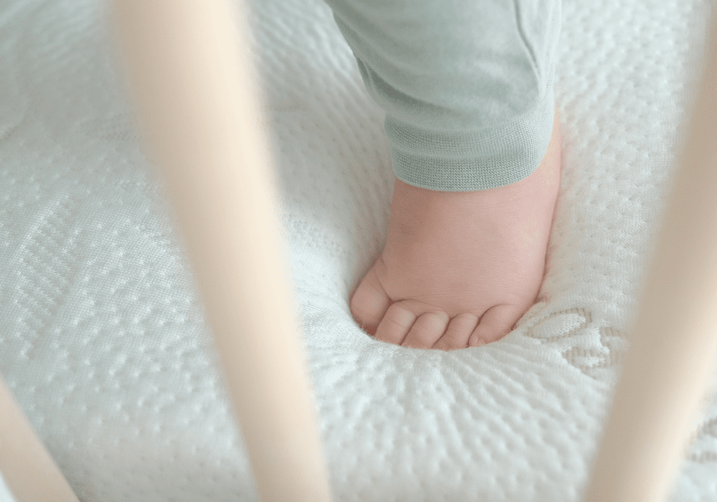 Soft steps, safe sleep: Baby's foot resting on a natural and certified Heveya® latex mattress.