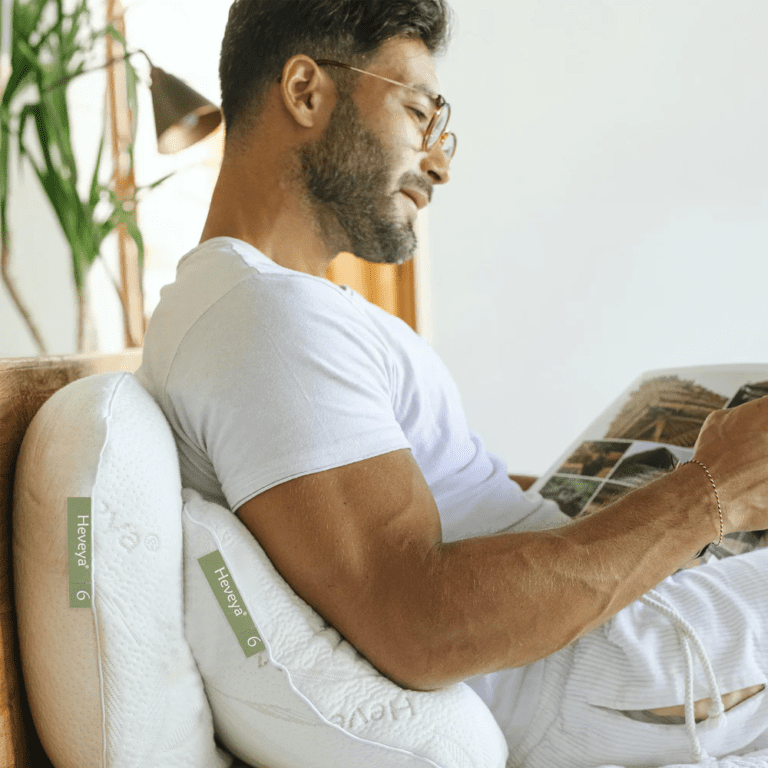 Man comfortably reading in bed with the Heveya Extra Firm Pillow for Side Sleepers. This versatile, supportive pillow offers maximum comfort for sleeping and reading.